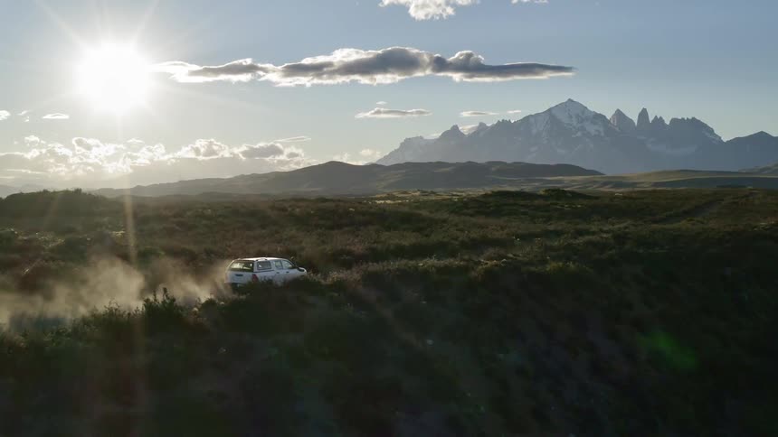 White vehicle travels on a dirt road under a blue sky