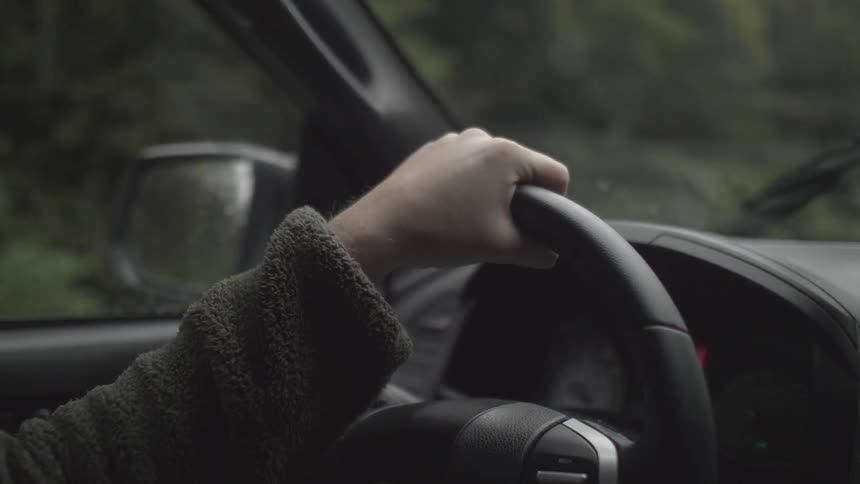 Person gripping steering wheel in car with windshield wipers on