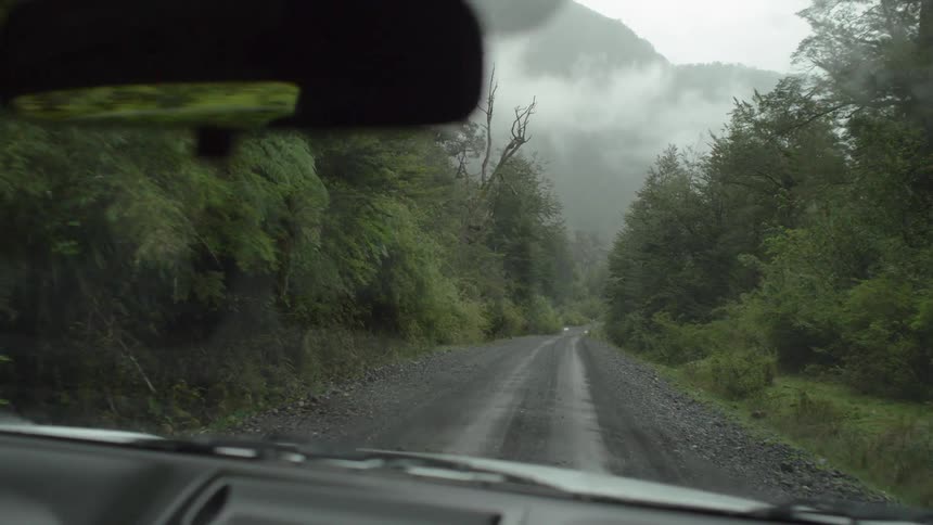 Car drives through gravel road to the distant foggy mountains in the forest