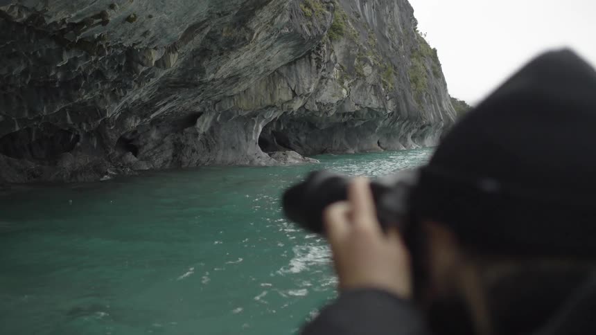 A person takes a photo of cliffs by the ocean as they stand near the water
