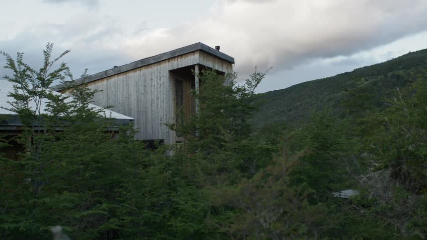A building stands in the forest surrounded by trees in front of a hill