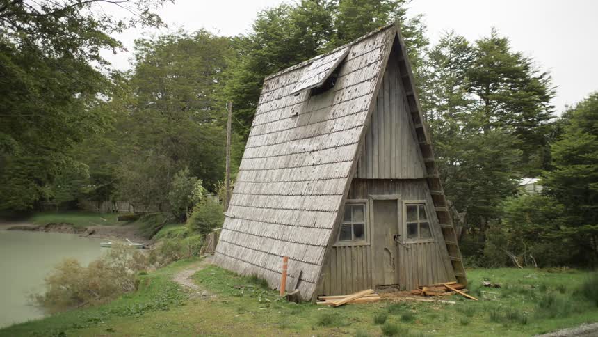 A small a frame structure sitting on the side of a body of water