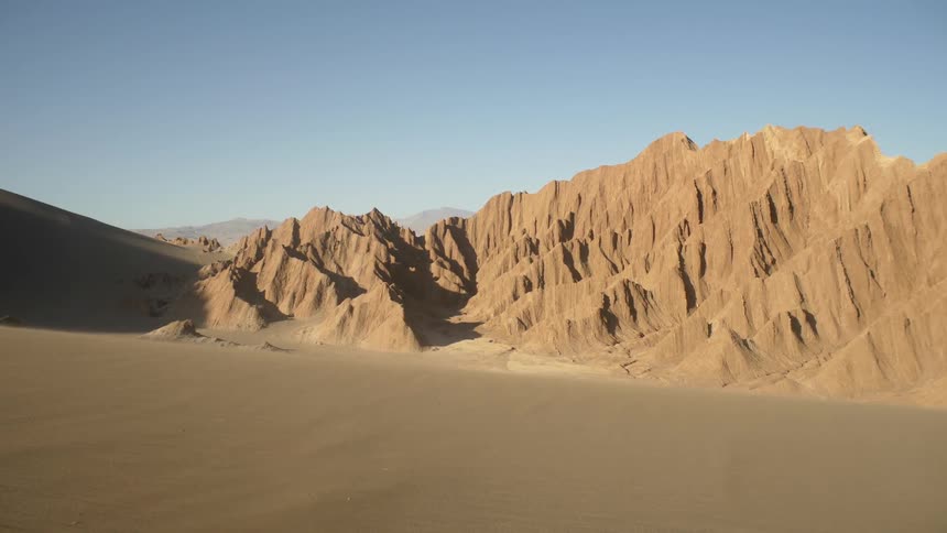 Sand and hills sit in the desert under a blue sky