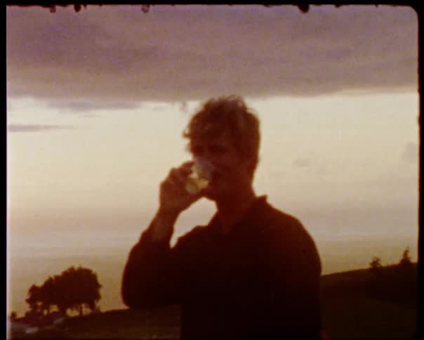 A man smiles and sips a drink at sunset