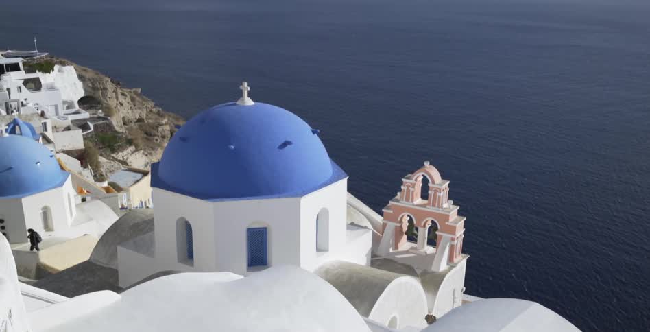 A man walks in between blue and white domed structures along the shoreline
