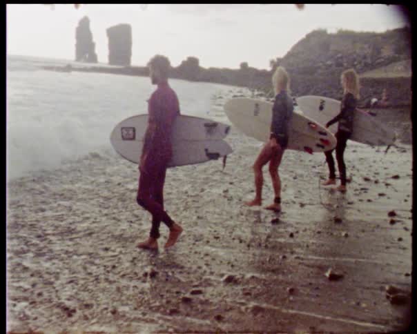 Three people walk towards the ocean carrying surfboards