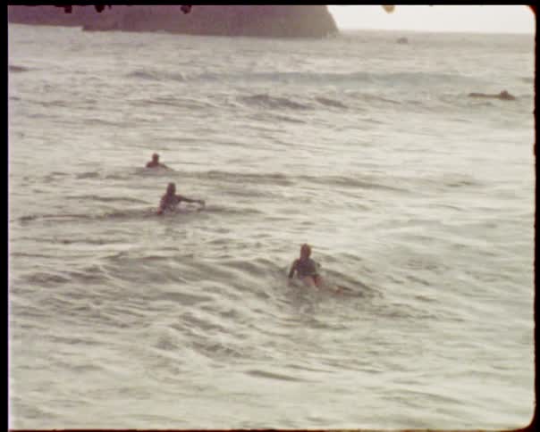 People paddle on surfboards in the ocean in a vintage home video
