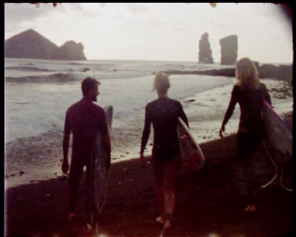 3 kids walking on a beach toward the water holding surfboards