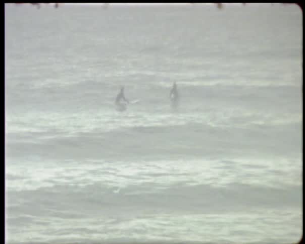 Surfers sit on their boards in the ocean bobbing up and down on the waves