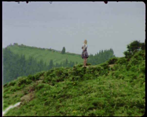 A woman stands on a hill covered in green vegetation