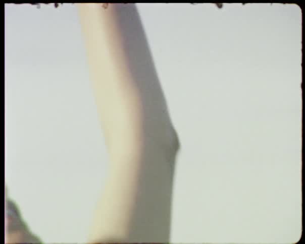 A woman wearing a bathing suit and a seashell necklace reaches up to the sky