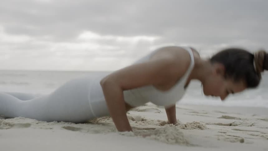A woman does burpees in the sand on the beach