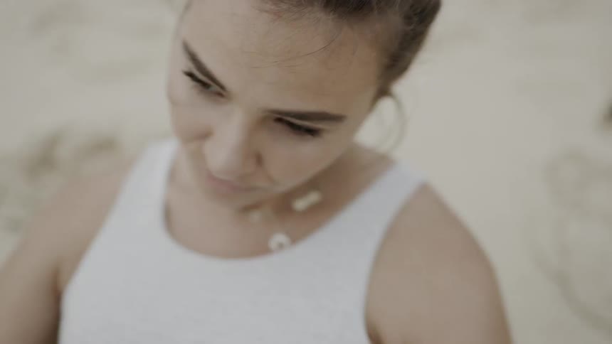 Woman who wears necklace does side sit ups on the white sand beach by day