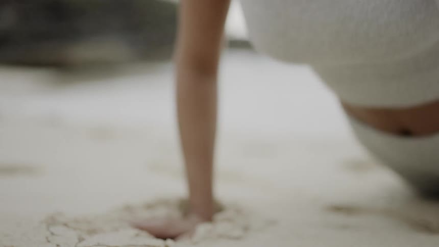 A woman does push ups on the sand of a beach