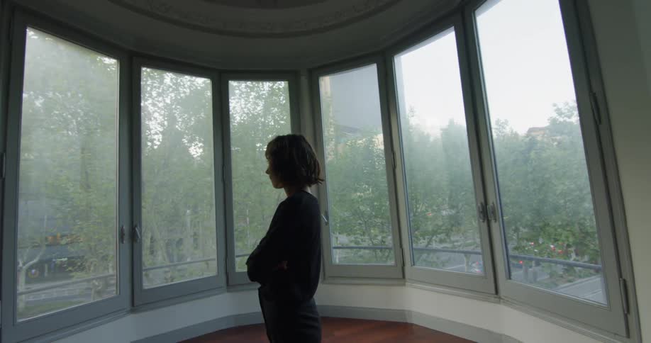 A woman stands in front of a curved wall of windows