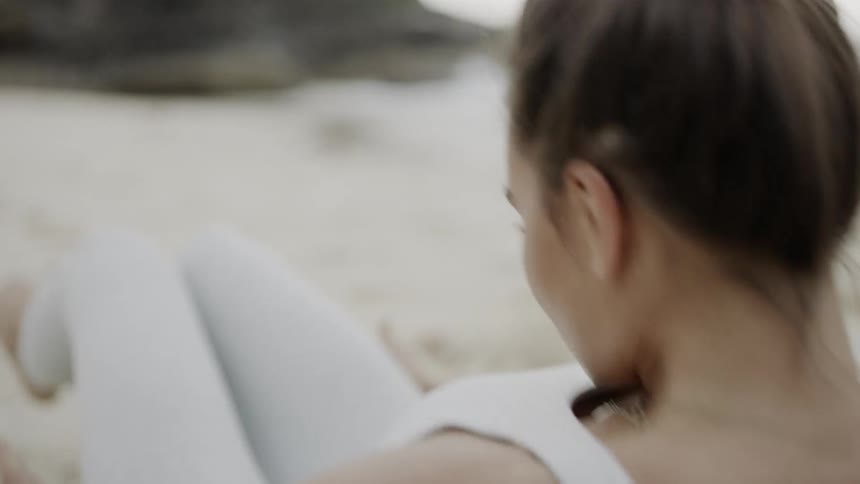 Woman does sit ups on the white sand beach by day