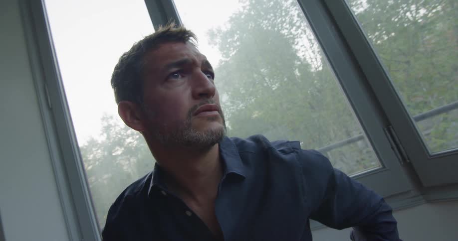 Man looks out the window with a state of sadness indoors by day
