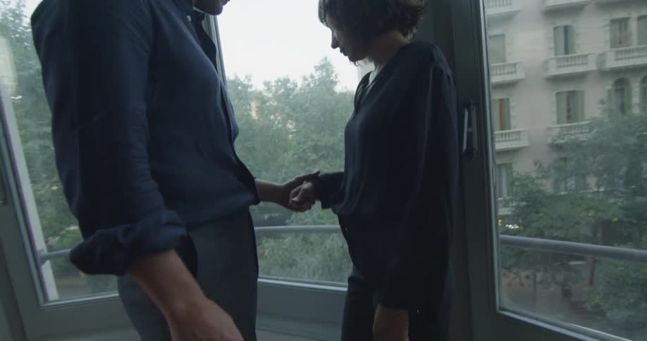 A man taking a woman's hand while standing near a large window on the second story during the day