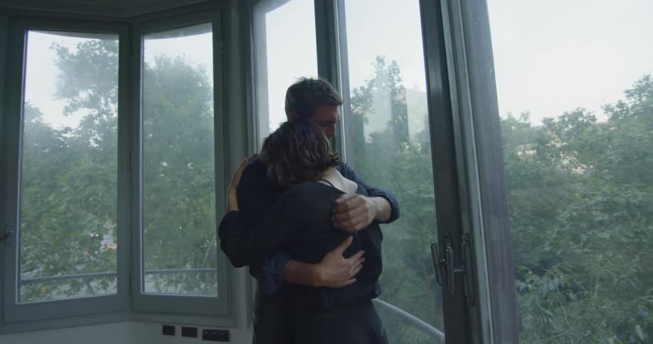 A man and woman hugging inside a window filled room
