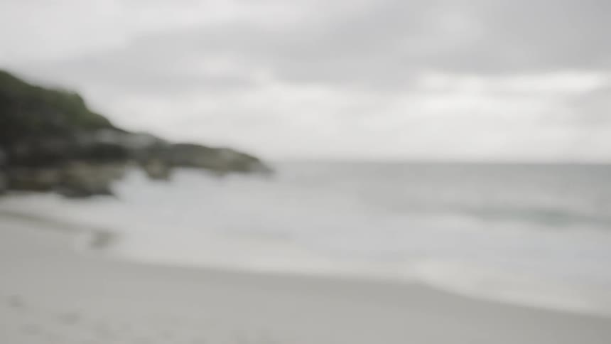 Woman works on on the white sand beach next to the sea on a cloudy day