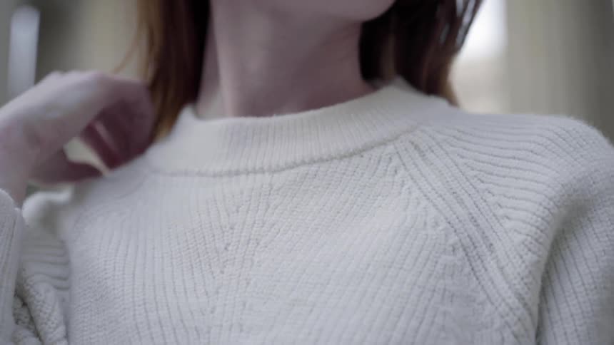 A woman wearing a white sweater fixes her hair