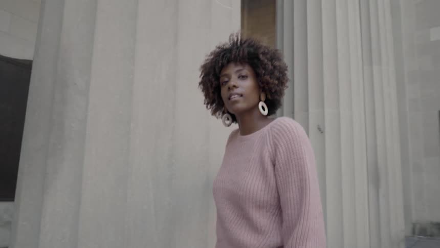 A black female walking around pillars of a building