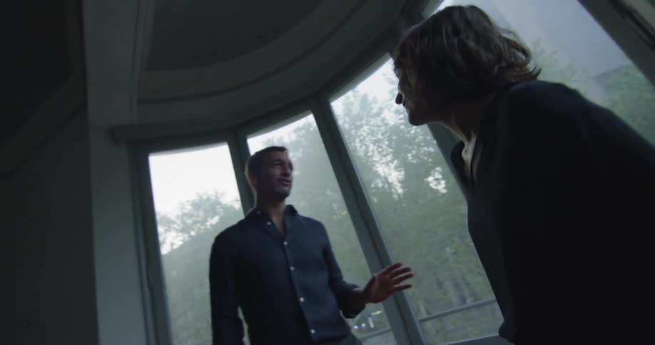 Couple laughing and talking while standing in around shaped room with lots of windows