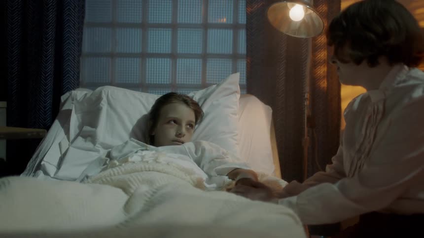 A woman sits and holds the hand of her daughter that is in a hospital bed and caresses her hair