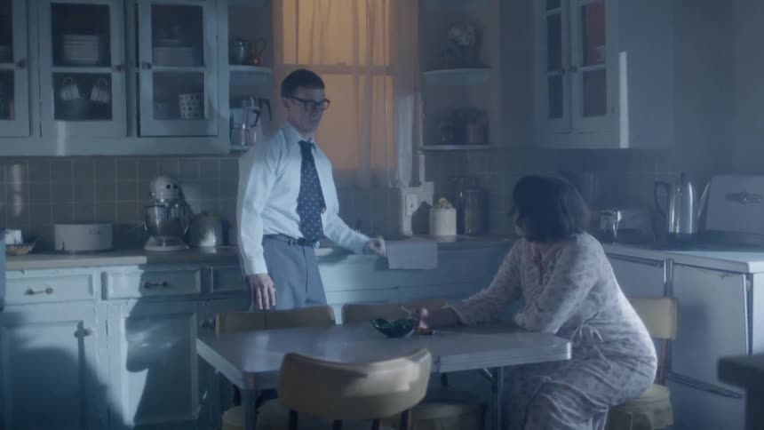 A woman smoking at a kitchen table arguing with a young man wearing a suit