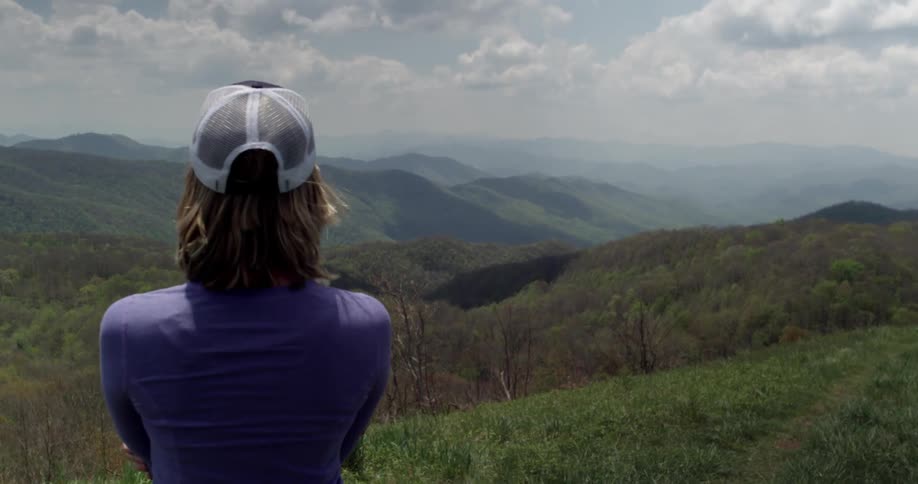 A woman stands at a mountaintop looking outwards