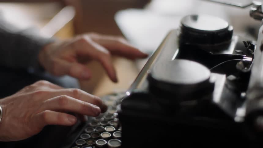A man sitting and typing on an old fashioned typewriter