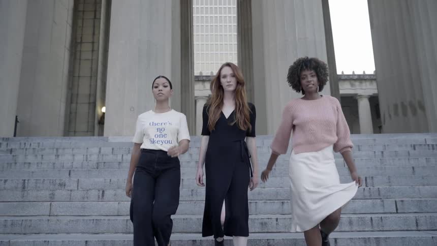 Three females walk next to one another down cement steps with huge pillars behind them