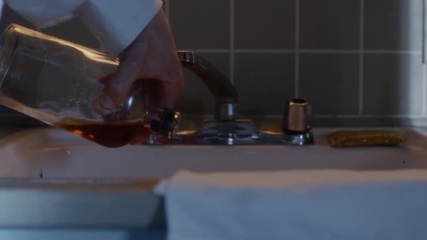 A man pouring liquor out of a bottle and down a sink drain