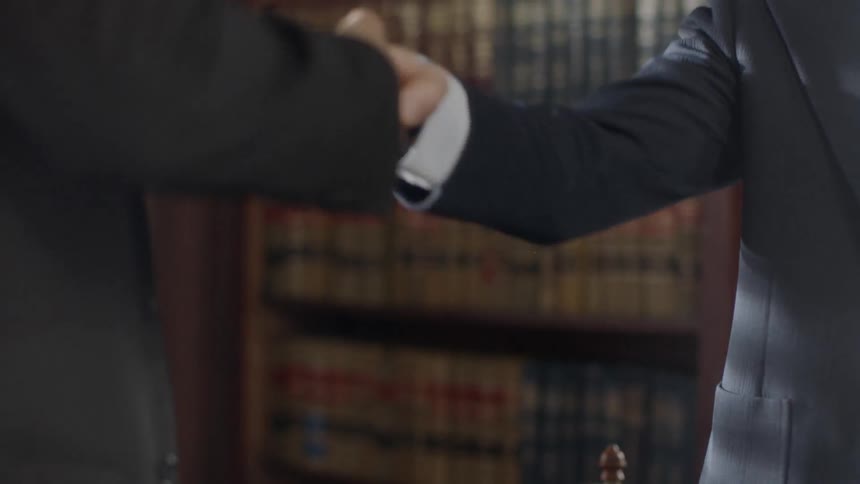 Two men wearing suits shake hands next to a globe