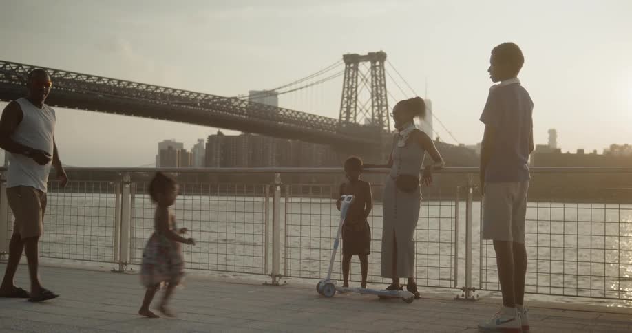 A black woman in a neck brace waiting with a child against the railing at a riverside