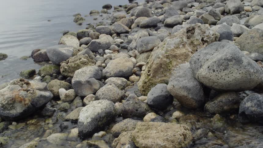 A stream trickles through rocks and into a large lake