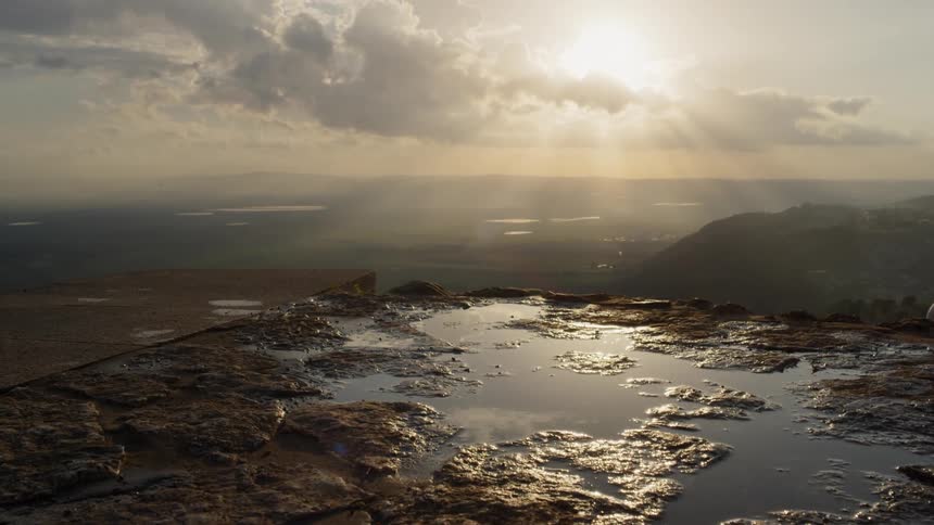 High above a valley a muddy mess is seen on a ledge following a rain as the sun begins to shine through the clouds in the sky