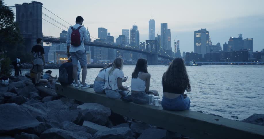 A group of people sit next to a Brooklyn waterfront overlooking a skyline