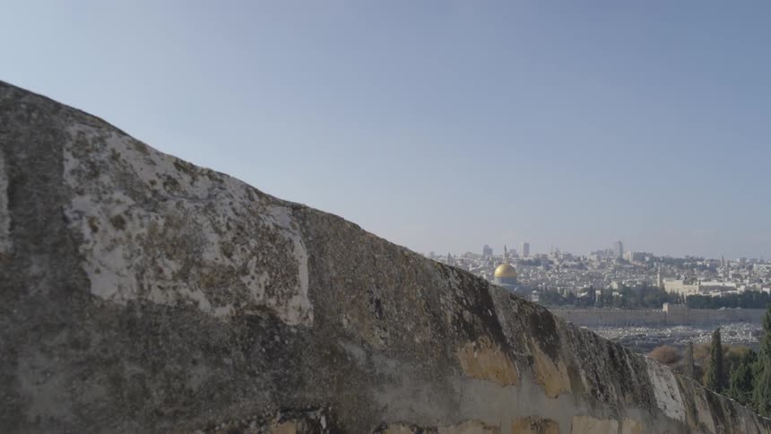 A golden dome in a city is visible over a stone wall on a slope