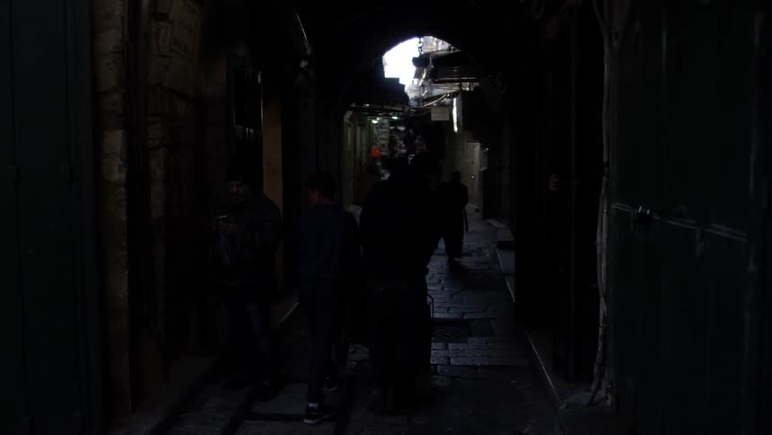 Several people walk down a dark alley