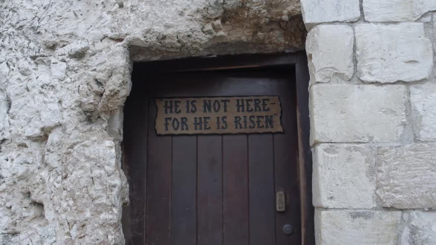 A wooden door with he is not here for he is risen resides within a stone wall