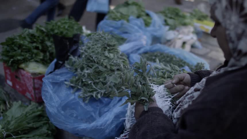A woman is sitting and tying herbs together as people walk past