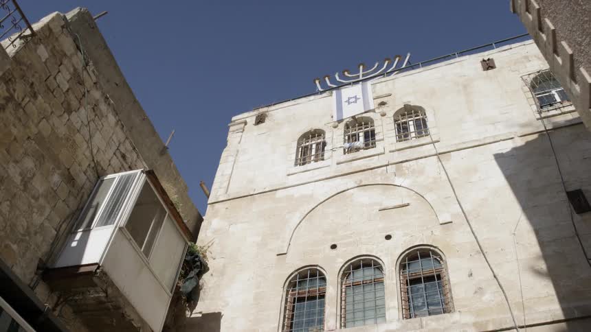 A stone jewish synagogue stands next to a clothing store