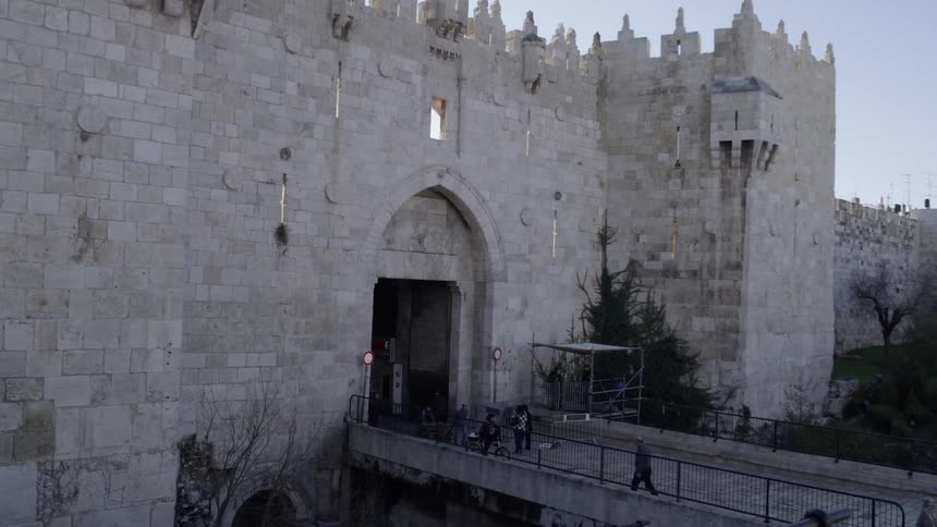 People walk and ride bicycles on the bridge into an old stone fort
