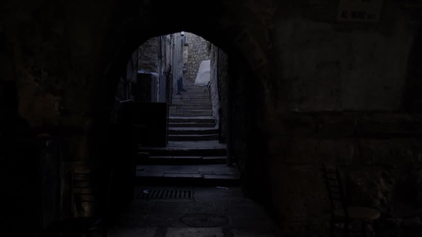 A very darkened alleyway is in between many old stone and brick buildings in what appears to be an old neighborhood