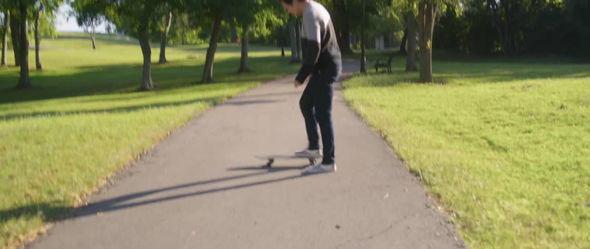 Man gets on skateboard in paved path at park