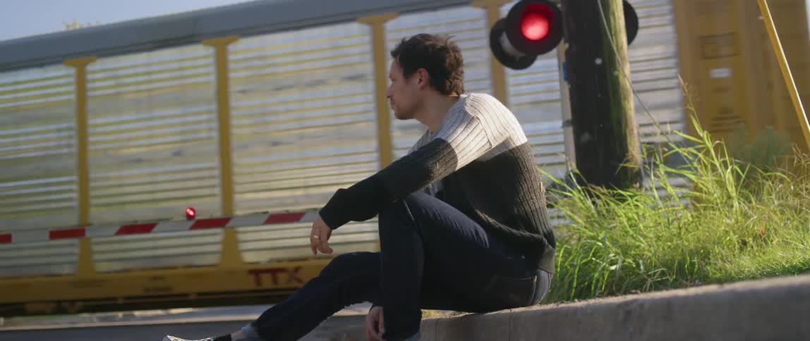 A man in a sweater sits at a railroad crossing while a train drives by