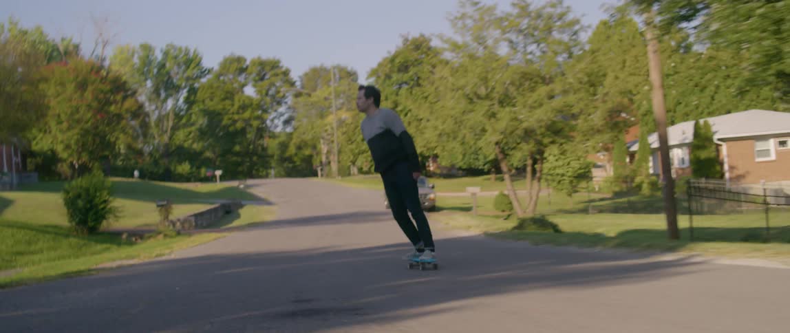 A man skateboards down a neighborhood street on a sunny day