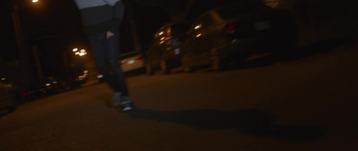 A man pushes off and rides his skateboard past parked cars on a neighborhood street
