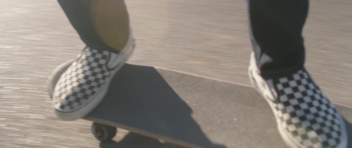 A skateboarder wearing checkered vans rides on a neighborhood road on a sunny day